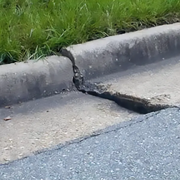 A crack on the sidewalk beside a grassy area.