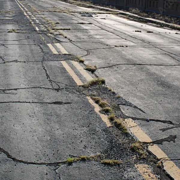A damaged road with numerous cracks and potholes.