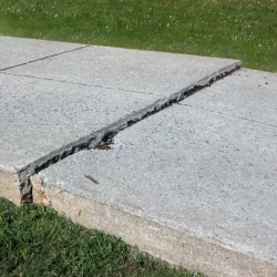 Cracked concrete sidewalk outside commercial apartment complex.